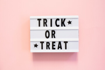 Halloween flat lay of lightbox with Trick or treat text and decoration over pink background. Holiday greeting card, party flyer, invitation concept