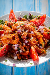 Penne with pork, tomato sauce, parmesan cheese, basil and vegetables served on wooden table
