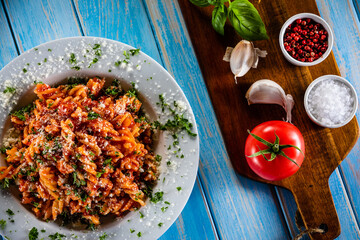 Fisilli with pork, tomato sauce, parmesan cheese, basil and vegetables served on wooden table
