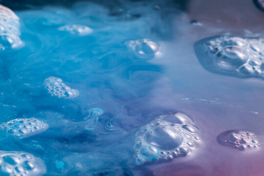 Blue and purple acrylic paint flowing in water creating lots of bubbles and droplets and other efects.