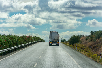 Fototapeta na wymiar Truck with silo for the transport of powders circulating on the highway on the edge of the horizon with a sky with clouds.