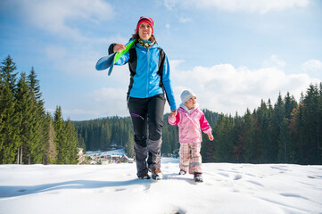 Mother and daughter walking up a ski slope.