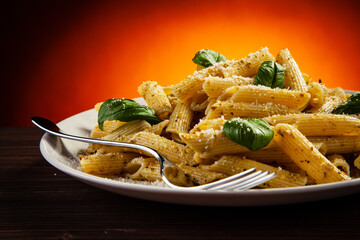 Penne with parmesan and basil on wooden table against gradient orange background 