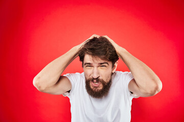 Emotional bearded man gestures with his hands in a white T-shirt aggression discontent red...