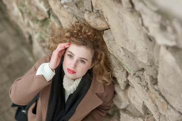 Portrait of a beautiful young woman near a stone wall. Looks up into the camera. Outside. View from above