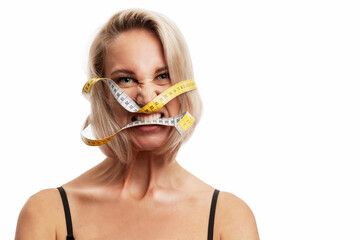 Angry young blonde woman with a measuring tape in her mouth. Isolated on white background. Space...