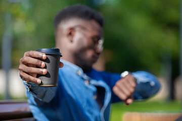 Close up of a coffee cup stretched by a busy african office worker looking at his watch