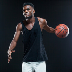 Portrait of afro american male basketball player playing with a ball over black background. Fit young man in sportswear holding basketball