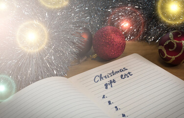 Festive concept, glittering Christmas baubles and a gift list on lined paper. An English text handwritten in a paper notebook "Christmas gift list"