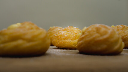 Mini cream puff or profiterole with dusting powdered sugar on a wooden background. It is a pastry ball fill with whipped cream and custard. Selected focus on foregrounds.