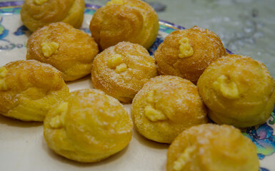 Mini cream puff or profiterole with dusting powdered sugar on a wooden background. It is a pastry ball fill with whipped cream and custard. Selected focus on foregrounds. Image contain bit of noise.