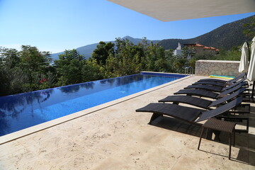 Beautiful infinity pool at the luxury villa in Turkey. Swimming pool with black sun chairs.