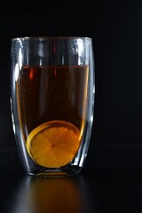 A glass of tea with a slice of lemon on a dark background with a light