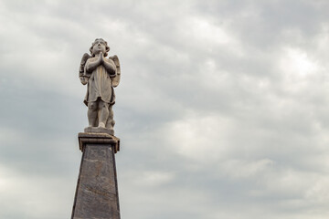 Escultura de anjo no topo de mausoléu com céu nublado ao fundo. Fotografia feita dentro do Cemitério Santana na cidade de Goiânia. 