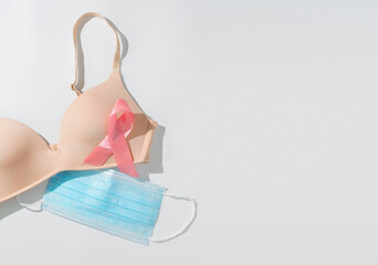 Pink ribbon with bra and hygienic mask for breast cancer awareness on white background. Cancer awareness concept.