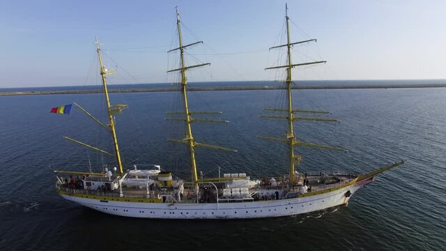 Aerial side view of a navy training ship near the coastline on a sunny day in the Black Sea. Three-masted bark/barque type with square rigging. Romanian flag