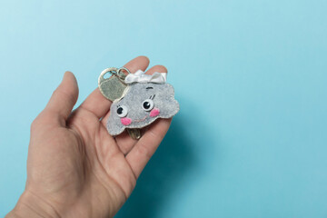 Felt keychain shaped of a funny cloud is in the girl's hand on a blue background. The key to the house is safety, property insurance.