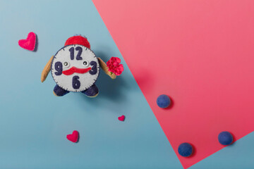 Cute felt alarm clock with a bouquet of flowers on a blue background with hearts. The concept of gifts. Copy space.