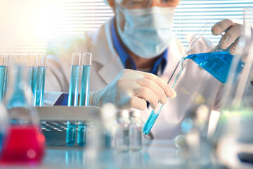 Scientist in laboratory pouring blue liquid from a beaker into a test tube