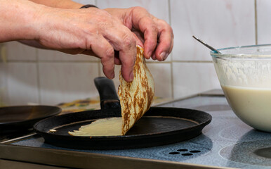 The woman's hands pour the pancake batter into a hot pan and fry them on both sides, turning them...