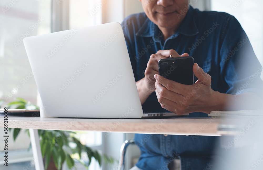 Poster asian business man using mobile smartphone during working on laptop computer on table in office