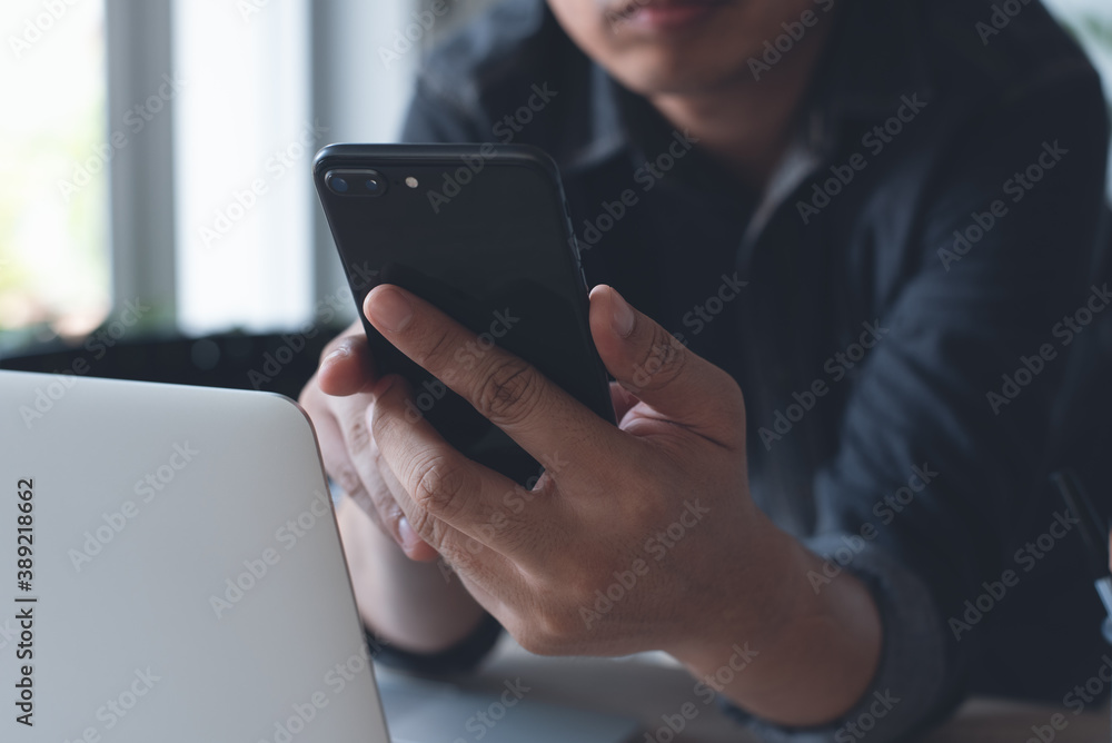 Poster close up of man hand using mobile phone during working on laptop computer in office