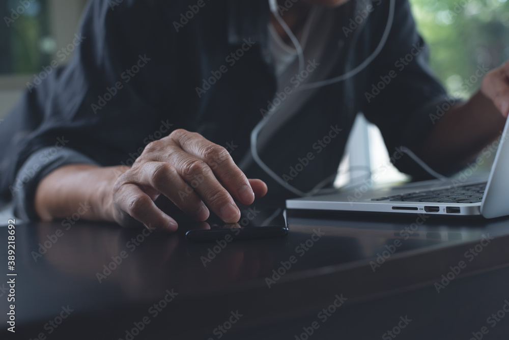 Poster man with earphones working on laptop computer and using mobile phone on office table