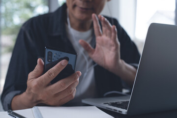 Man making facetime video call via mobile phone during working on laptop computer in office