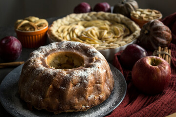 Apple pies of different types on a table with fresh fruits, cinnamon sticks and pumpkins. Autumn  menu ideas. Homemade dessert close up photo. 
