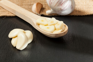 Garlic - Allium sativum; Wooden spoon with garlic; photo on a dark background.