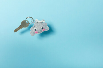 Felt keychain shaped of a funny cloudand key are on a blue background. The key to the house is...