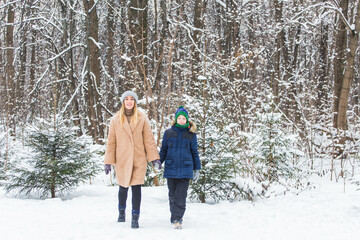 Portrait of happy mother with child son in winter outdoors. Snowy park. Single parent.