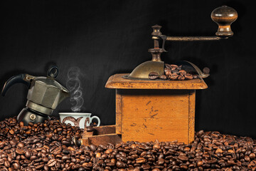 Old manual coffee grinder, Italian coffee maker and a cup on a pile of roasted coffee beans with empty blackboard in the background. - Powered by Adobe