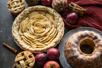 Apple pies of different types on a table with fresh fruits, cinnamon sticks and pumpkins. Autumn  menu ideas. Homemade dessert close up photo. 
