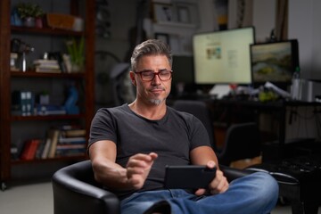 Man using smart phone at home sitting in armchair in cosy living room.