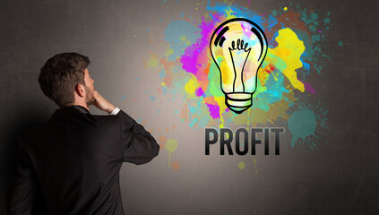 businessman drawing colorful light bulb with PROFIT inscription on textured concrete wall, new business idea concept