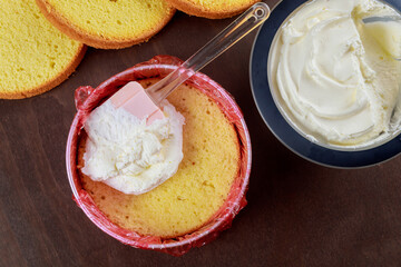 White icing in bowl with spatula and round sponge cake.