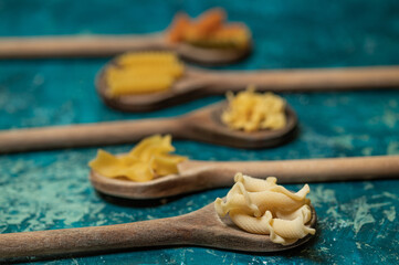 Various mix of dry pasta on wooden spoons.