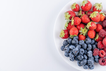 Fresh berries raspberries, strawberries and blueberries in plate isolated on white background, top view with copy space