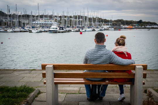 Couple sits on the bench in harbor looking at yachts. Relaxing atmosphere