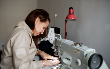 A woman sews a dark fabric on a sewing machine. Design studio, tailoring process concept.