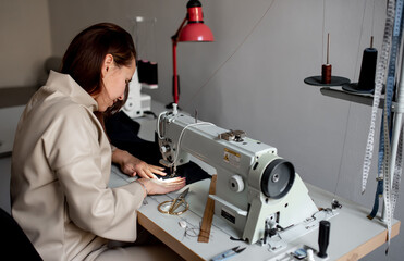A woman sews a dark fabric on a sewing machine. Design studio, tailoring process concept.