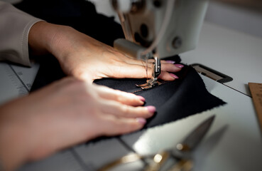 A woman sews a dark fabric on a sewing machine. Design studio, tailoring process concept.