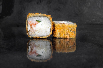 Tempura rolls with salmon, cucumber, eel and cream cheese on a dark background with reflection