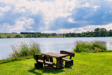 Picknickbank mit Tisch am See im Hintergrund Hügel und Bäume im Sommer  