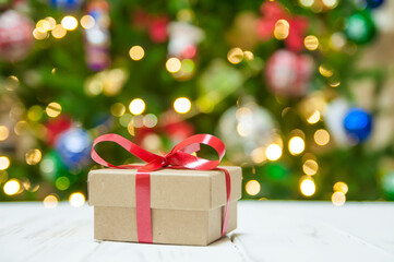 gift box with a red bow on the background of blurred lights of the Christmas tree