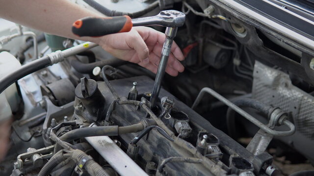 A man unscrews an old spark plug from a car engine with a tool