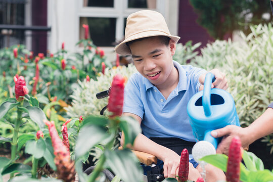 Asian special child on wheelchair watering the plants in flower garden,Daily activities happiness with family time in the home,Lifestyle in the education age and happy disabled kid with earth concept.