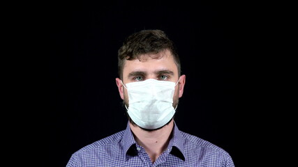 A man in a medical mask coughs heavily on a black background
