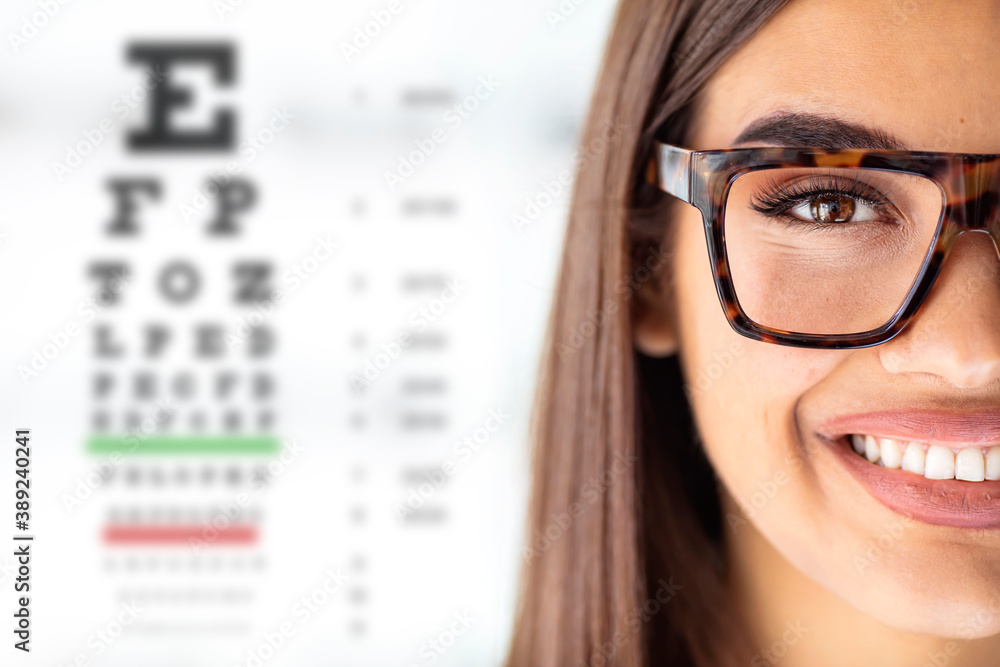 Wall mural close up of young woman wearing eyeglasses with eyechart in the background. eyewear. closeup view of